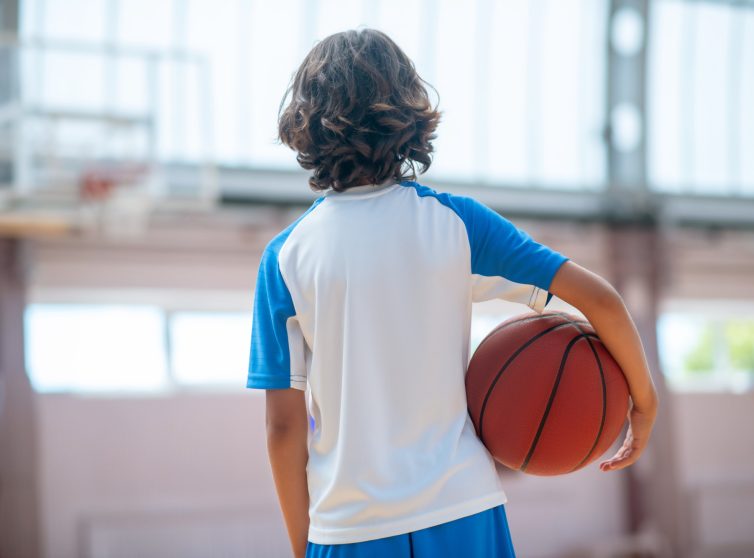 Child holding basketball at hip facing hoop